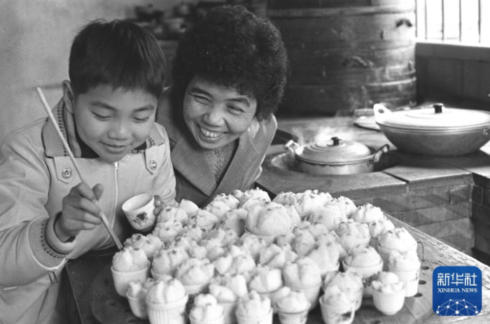 1980年，福建泉州归侨陈素珍教她的小儿子在年糕上点红。春节时蒸年糕是福建侨乡的习俗，象征在新的一年里生产和生活要步步高。新华社记者 郑震孙 摄